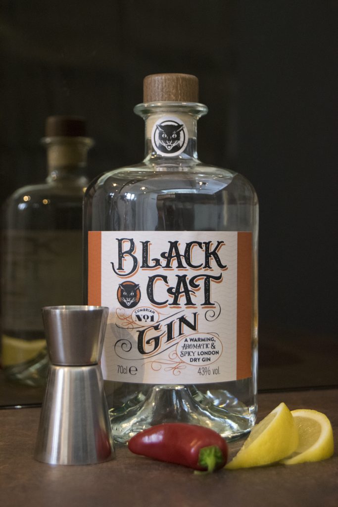 Bottle of Black Cat Spicy Gin Cumbrian No 1 with a wedge of lemon and jalapeno in the foreground.