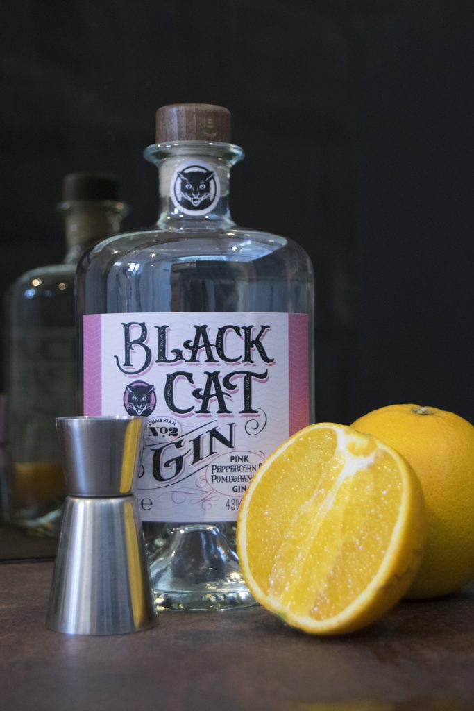 Bottle of Black Cat Fruity Gin Cumbrian No 2 with half an orange and jigger in the foreground
