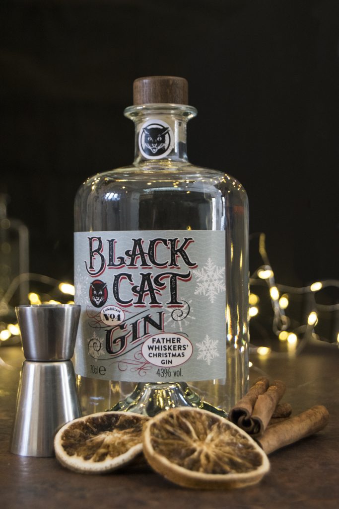 Bottle of Black Cat Father Whiskers Christmas Gin Cumbrian No 4 with sparkly lights behind